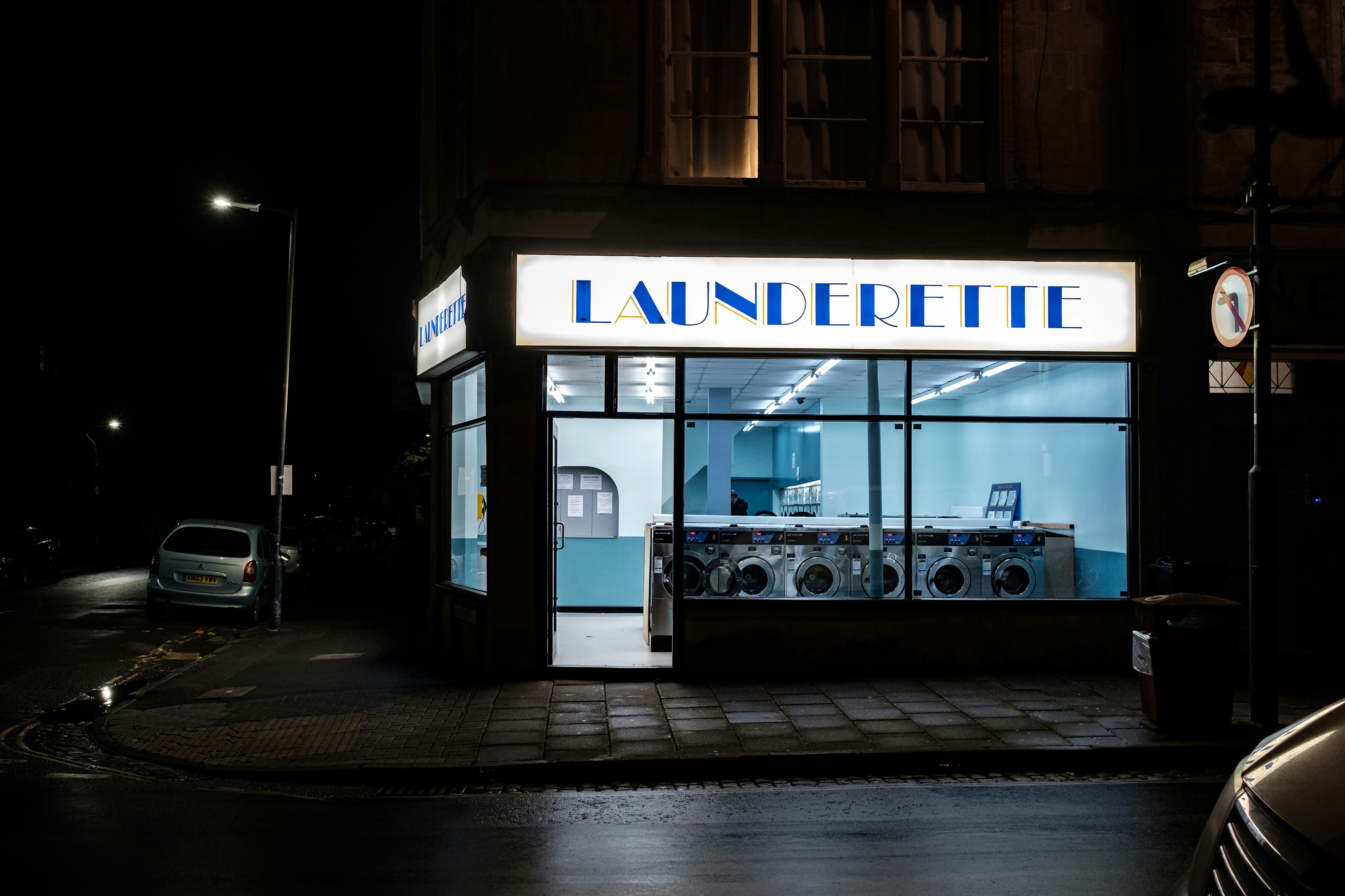 An empty laundromat at night, fluorescent-lit through plate glass.